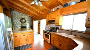 A kitchen with wooden cabinets, a stone wall, a built-in oven, and a large window. - Johnson Home Lake Front, Boat slip, walking distance to Pines. Takes Pets (Bass Lake)