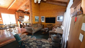 A cozy cabin interior with wooden walls, a dining area, a living room with a sofa and chairs, and a television. - Johnson Home Lake Front, Boat slip, walking distance to Pines. Takes Pets (Bass Lake)