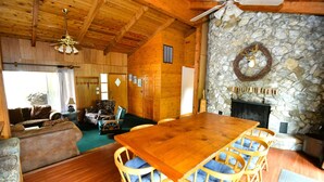 A wooden interior with a large dining table, stone fireplace, and a ceiling fan. - Johnson Home Lake Front, Boat slip, walking distance to Pines. Takes Pets (Bass Lake)