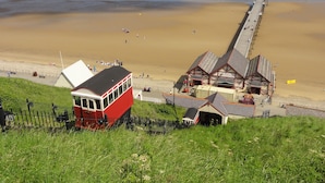 Eine Küstenansicht mit einem Steg, der sich ins Meer erstreckt, einem roten Bus und einem Gebäude im traditionellen Baustil.