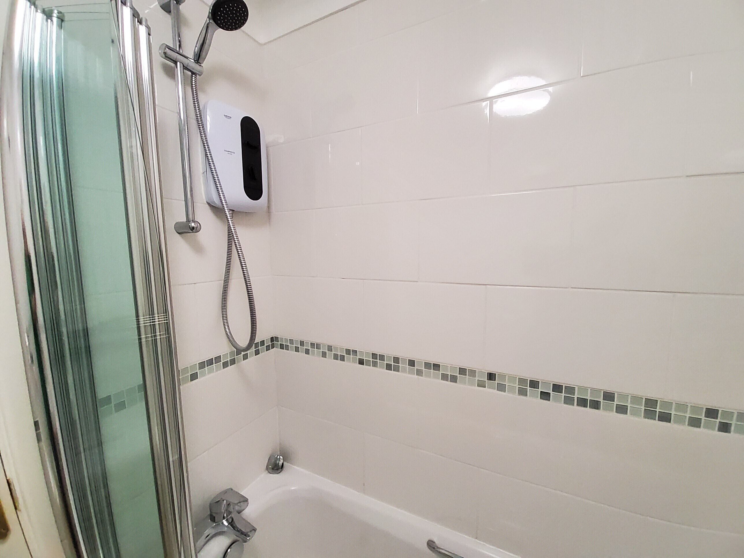 A bathroom with a glass shower enclosure, a handheld showerhead, a handheld dryer, and a bathtub.