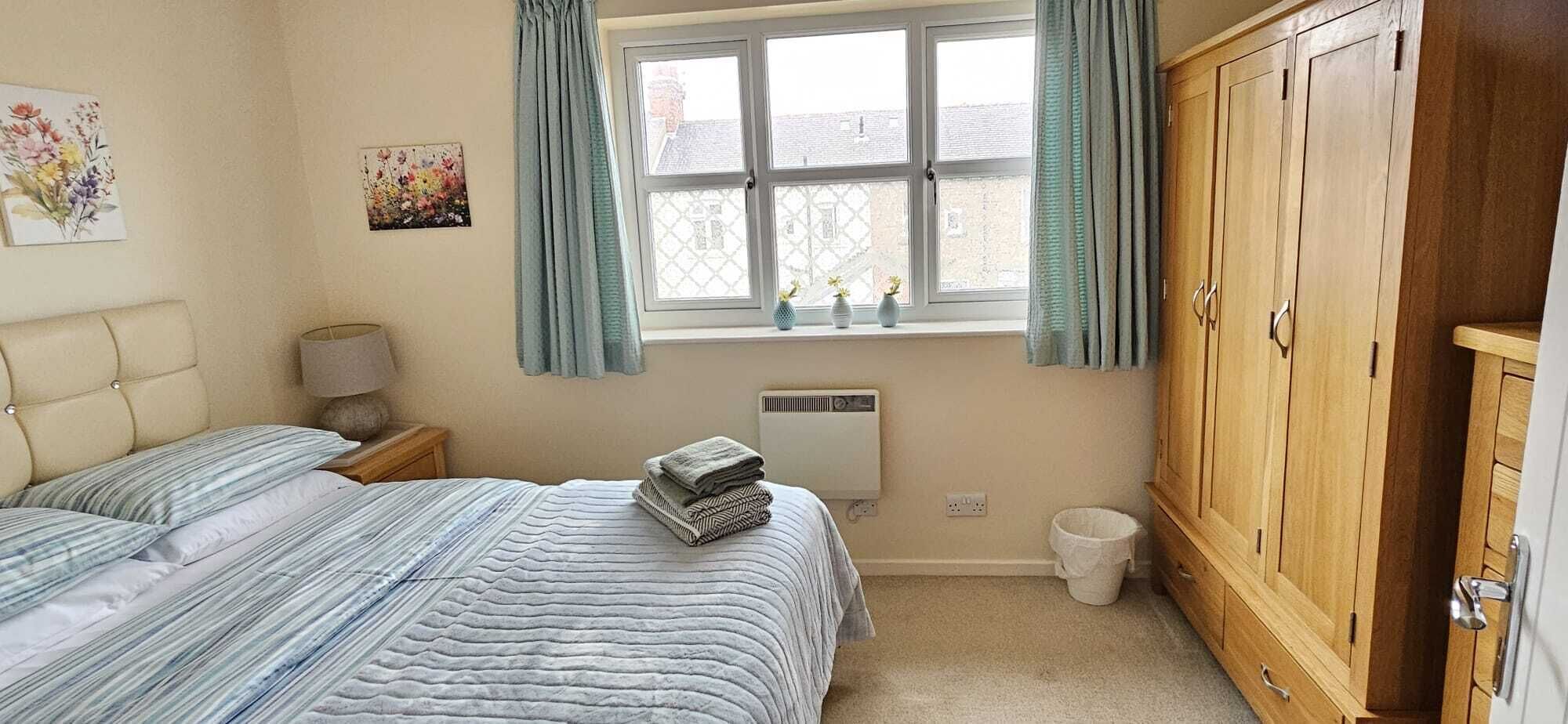 Ein Schlafzimmer mit einem Bett, einem Nachttisch, einem Fenster mit Vorhängen, einer Heizung und einem Holzschrank.