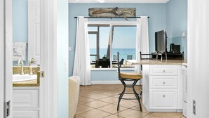 A kitchen with a view of the ocean, a ceiling fan, and a rustic wooden art piece above the window. - Beach House 3 · Ground Level · Door to Sand (Bradenton Beach)
