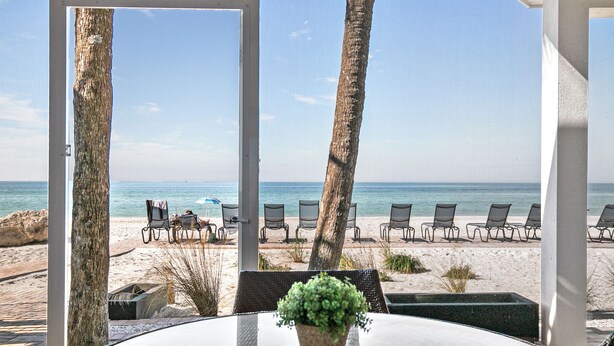 A beachside patio with a glass table, chairs, and a potted plant. - Beach House 3 · Ground Level · Door to Sand (Bradenton Beach)