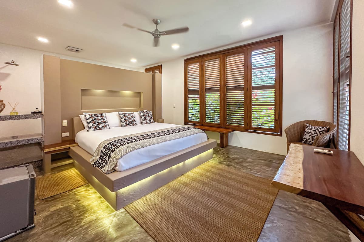 A modern bedroom with a large bed, a ceiling fan, and a window with blinds.