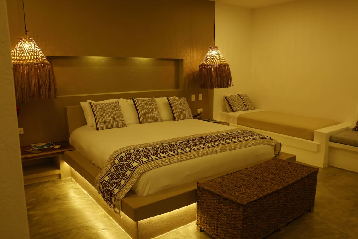 A modern bedroom with a large bed, bedside tables, a bench, and two hanging lamps.