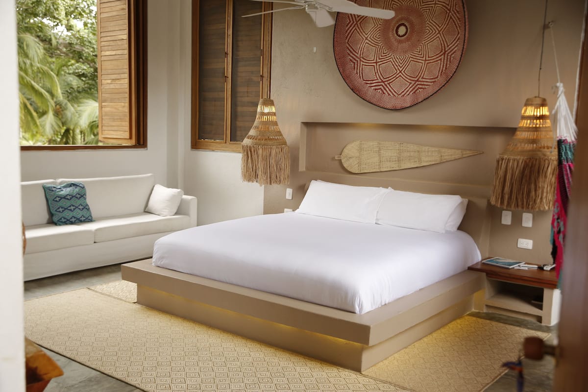 A modern bedroom with a large bed, a sofa, and a decorative wall hanging.