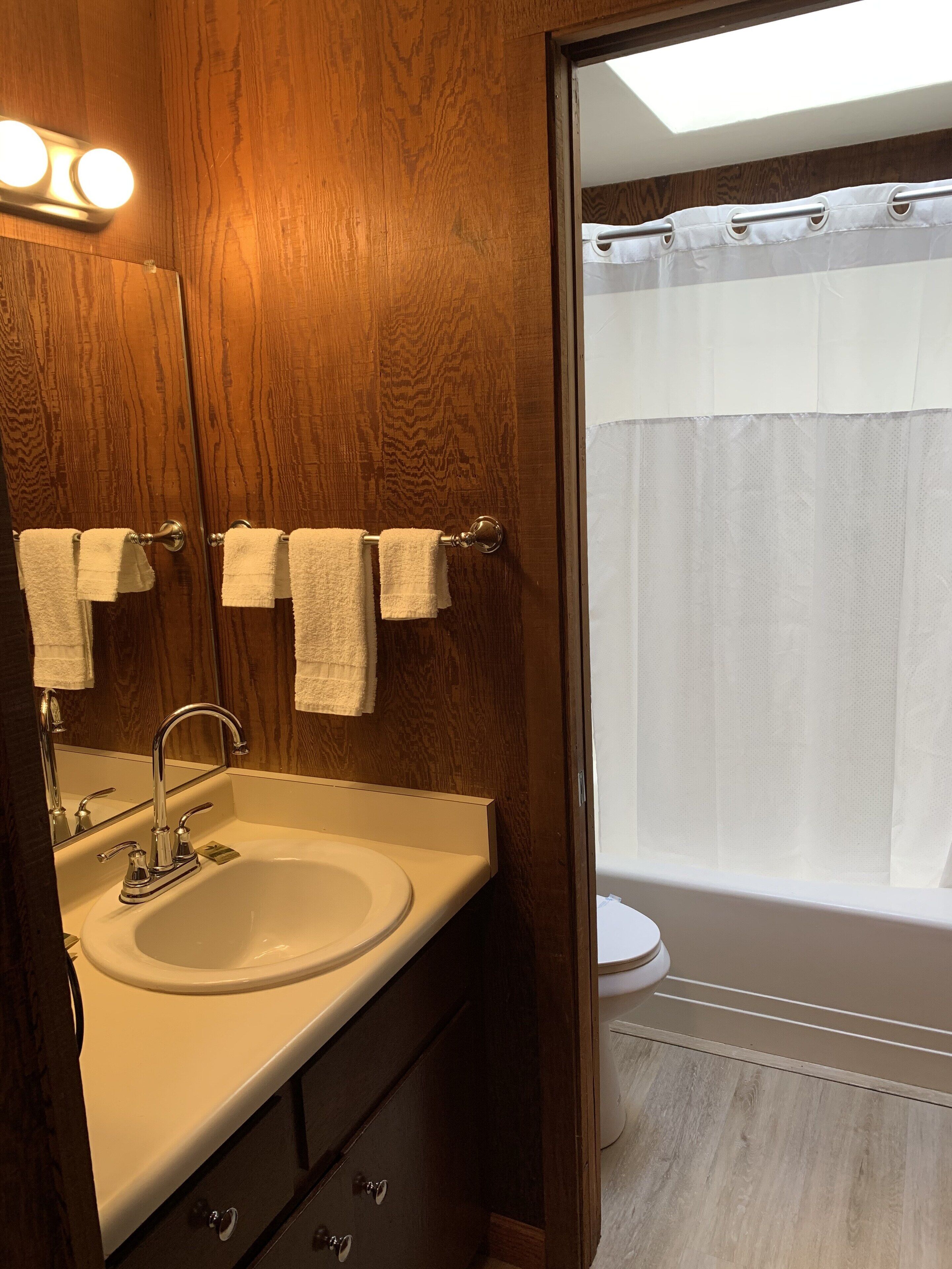 Un baño con tocador de madera, lavamanos, espejo y cortina de ducha.