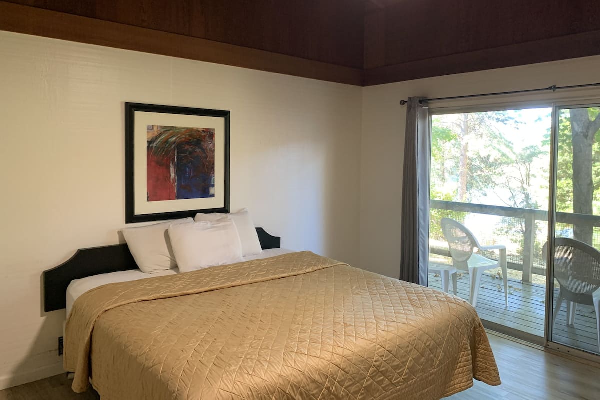 A bedroom with a bed, a ceiling fan, a framed artwork, and a view through a sliding glass door to an outdoor area with chairs.