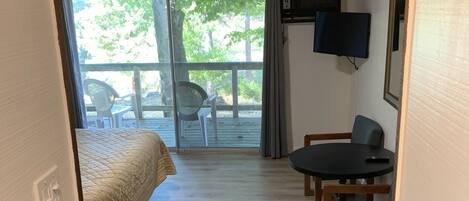 A room with a bed, a table with chairs, a television, and a view of the outdoors.