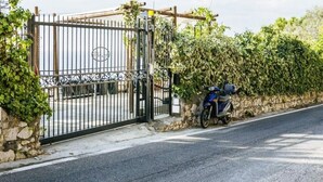 A gated entrance with a metal gate, a stone wall, and a motorcycle parked beside it.