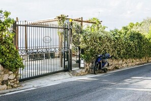 Ein verschlossenes Tor mit einem Metallgitter, einer Steinmauer und einem daneben abgestellten Motorrad.