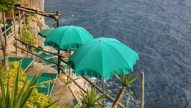 A coastal terrace with green umbrellas and lounge chairs overlooking the sea.