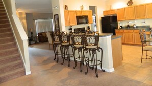 A kitchen with wooden cabinets, a black refrigerator, and a bar area with four chairs. - 7 Bed, 5 Bath. 15 Mins From Closest Disney Attractions (Orlando)