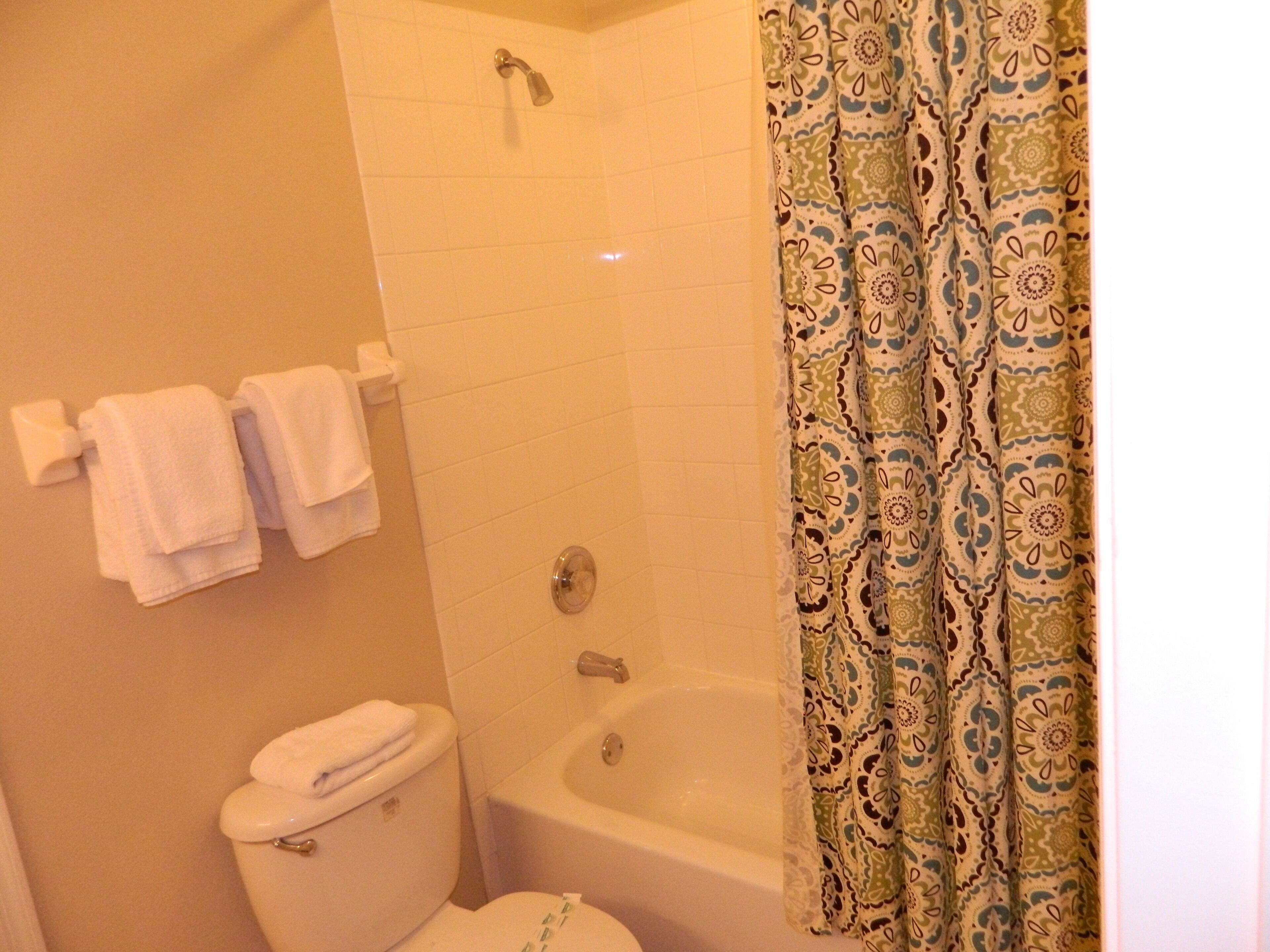 A bathroom with a toilet, a shower, and a bathtub. There are two white towels hanging on a rack.
