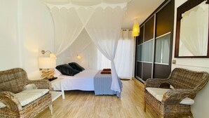 A bedroom with a canopy bed, two wicker chairs, a bedside table with a lamp, and a large window with curtains. - Casa mar i sol El Cotillo (El Cotillo)