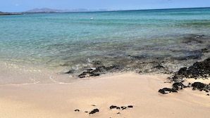 A beach with clear turquoise water, a sandy shore, and distant mountains. - Casa mar i sol El Cotillo (El Cotillo)