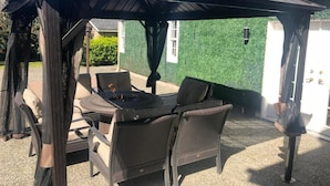 An outdoor patio with a covered seating area, a fire pit, and a green wall in the background. - Royalty B&B (Richmond)