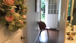 A hallway with a wooden floor, a white door, a red chair, and a decorative wall hanging. - Royalty B&B (Richmond)