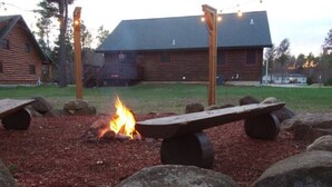 Eine hölzerne Bank mit einem Feuer in der Mitte, umgeben von Steinen, vor einem Chalet mit geneigtem Dach.