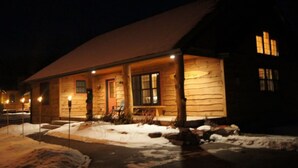 Eine Blockhütte mit verschneitem Vorbau und beleuchteter Fassade.