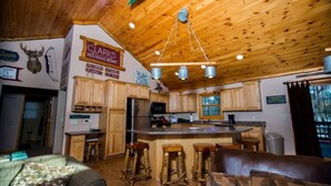 Ein rustikales Blockhaus-Interieur mit Holzwänden und -decken, einer zentralen Kochinsel mit Sitzgelegenheiten, einem Küchenbereich und einem Schild für 'Clark's Red Rock Resort'.