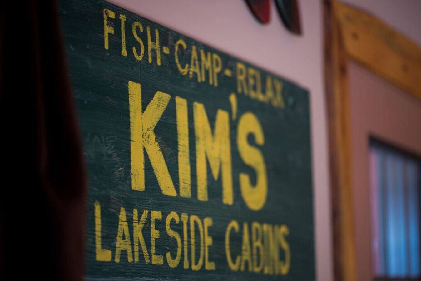 Une enseigne pour les chalets de Kim, situés au bord du lac, avec un texte indiquant qu’ils proposent des activités de pêche et un cadre propice à la détente.