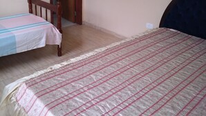 Ein Schlafzimmer mit zwei Einzelbetten, einem Holzsessel und einer Tür zu einem anderen Raum.