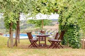 Un área de comedor al aire libre con mesa y sillas, rodeada de follaje y con vistas a una piscina.