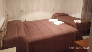 Habitación de hotel con dos camas, cada una con cubrecama y almohadas marrones. Se ven toallas dobladas sobre las camas. Las paredes son blancas y el cabecero es de madera.