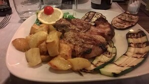 Un plato con carne a la parrilla, papas, calabacín a la parrilla y una rodaja de limón.