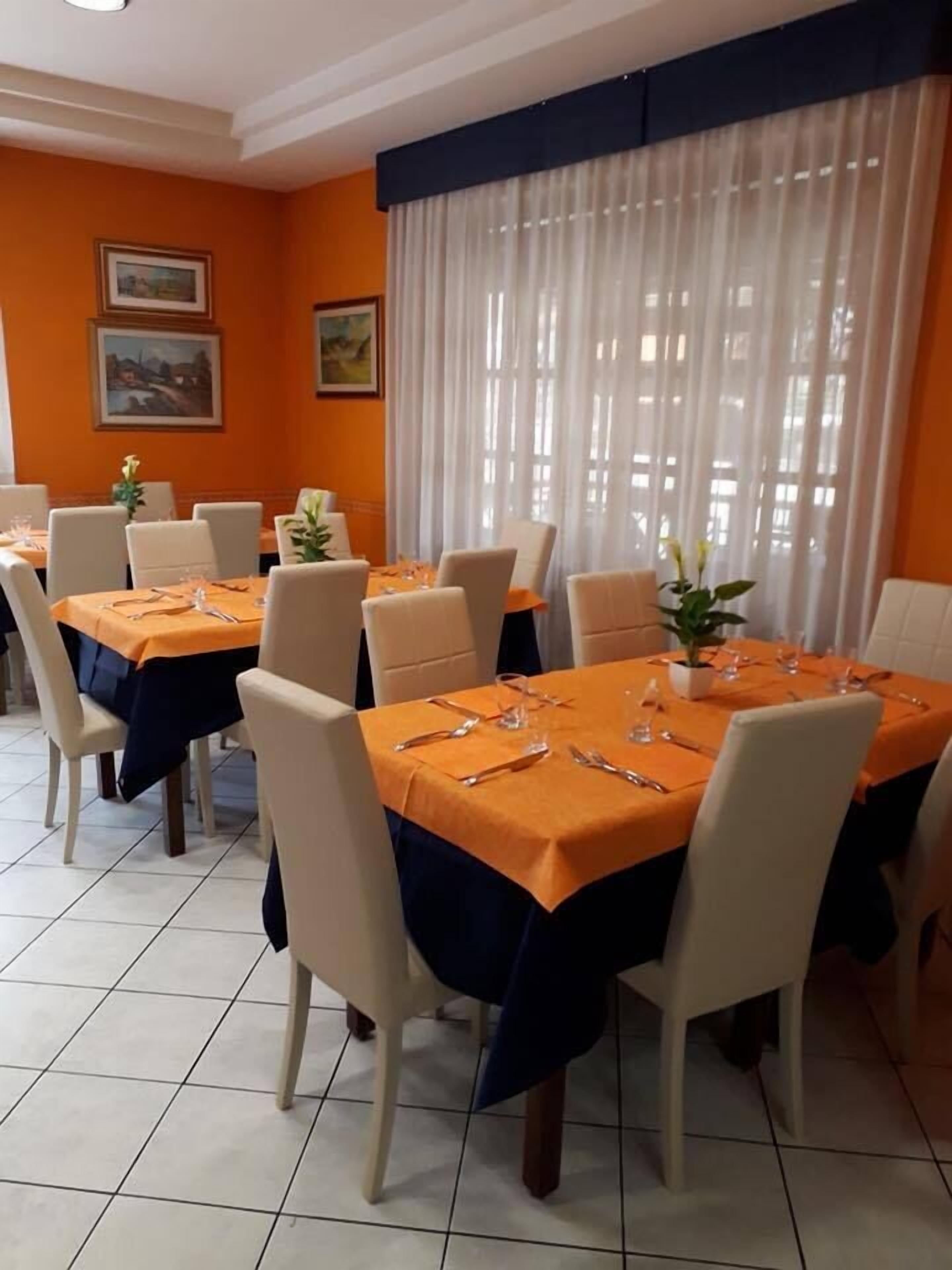 Un espace repas avec des tables dressées pour quatre personnes, des chaises blanches et des nappes orange.