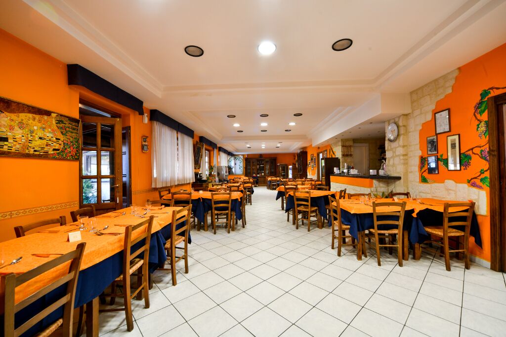 Une grande salle à manger avec de nombreuses tables et chaises, un sol carrelé et des murs orange.