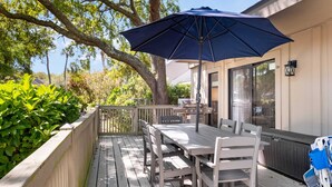 A wooden deck with a table and chairs, a blue umbrella, and a grill area.