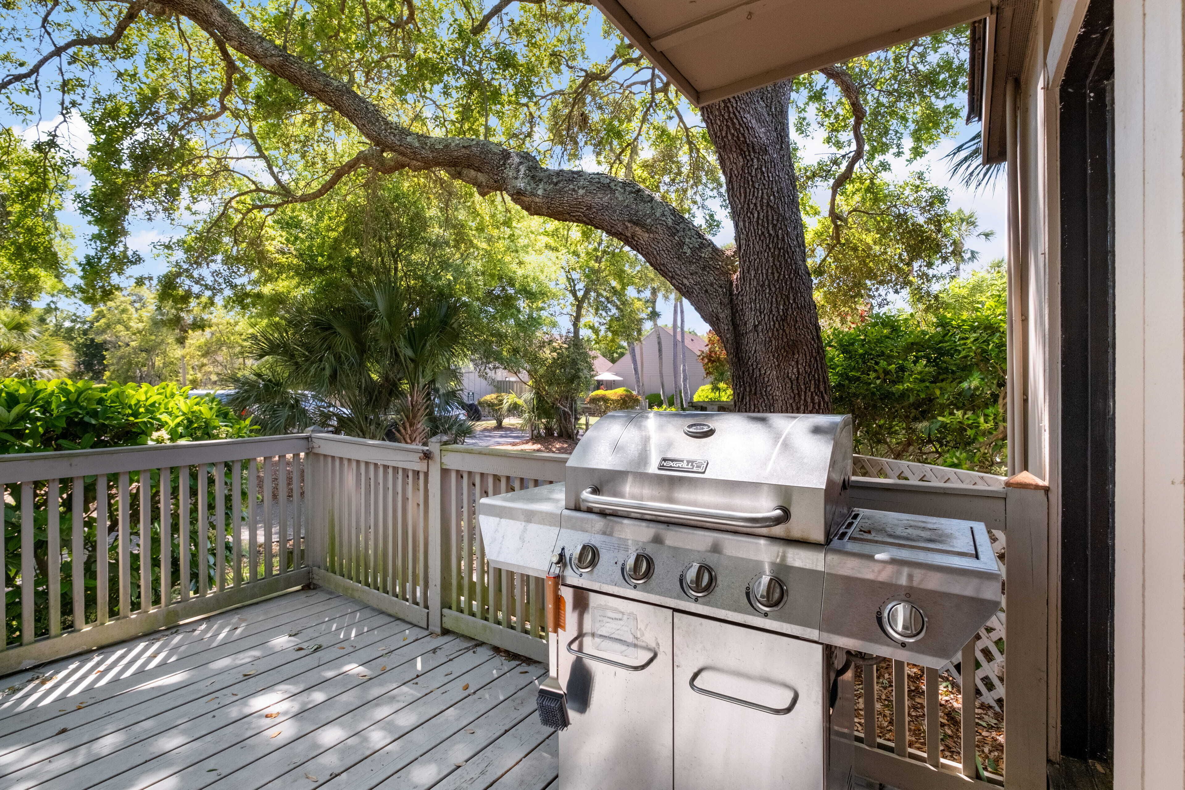 Un barbecue sur une terrasse en bois, avec une clôture blanche et des arbres en arrière-plan.