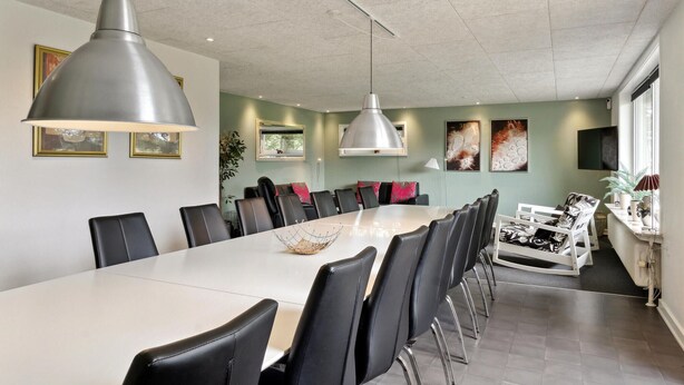 A modern dining area with a long table and black chairs, overhead pendant lighting, and artwork on the walls.