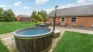 A backyard with a hot tub, a brick house, and a lawn.