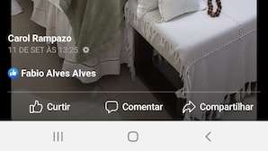 Un dormitorio con cama, almohadas, una cruz en la pared y un pequeño banco con cuentas.
