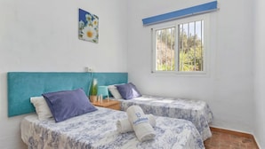 Une chambre avec deux lits, une fenêtre donnant sur un beau paysage, une tête de lit de couleur turquoise et une petite plante sur la table de chevet.