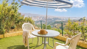Une terrasse avec une table ronde, deux chaises, un parasol à rayures et une vue sur le paysage urbain.