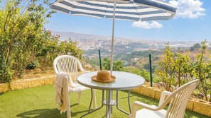 A patio with a round table, two chairs, a striped umbrella, and a view of a cityscape.