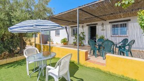 Un patio con una mesa y sillas, un paraguas a rayas y una zona de estar cubierta.