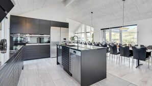 A modern kitchen with a central island, built-in appliances, and a dining area with chairs and tables. - Stunning home in Hvide Sande with sauna (Hvide Sande)