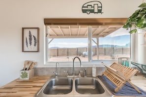 Enjoy a desert view from this kitchen with a double sink, wooden countertop, and a hanging chair.