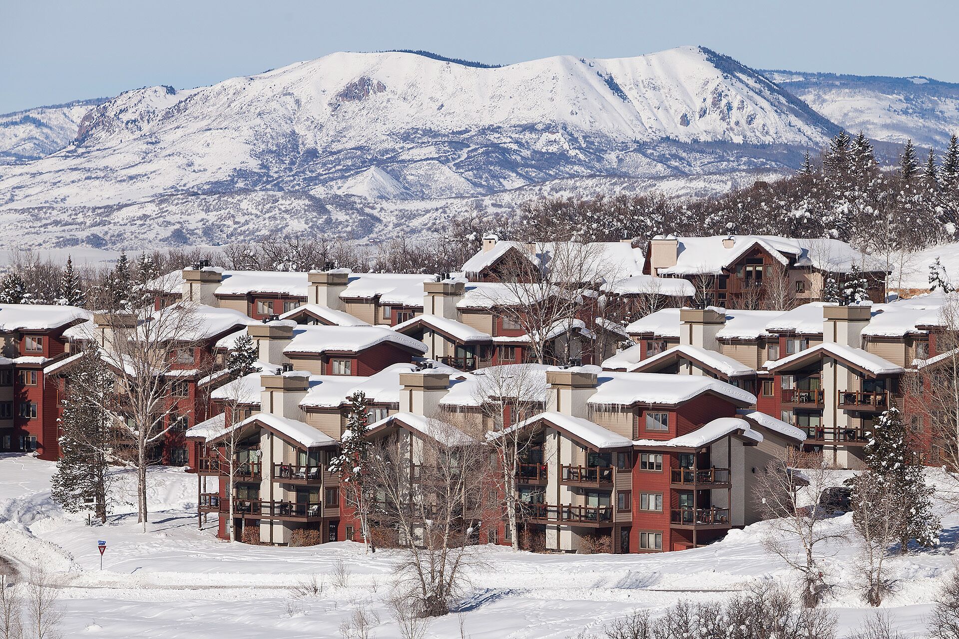 Estância de inverno coberta de neve com vários edifícios de dois andares, cada um com varandas e uma pista de esqui ao fundo.