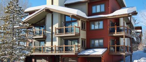 Un edificio de varios pisos con balcones, garaje y paisajes nevados.