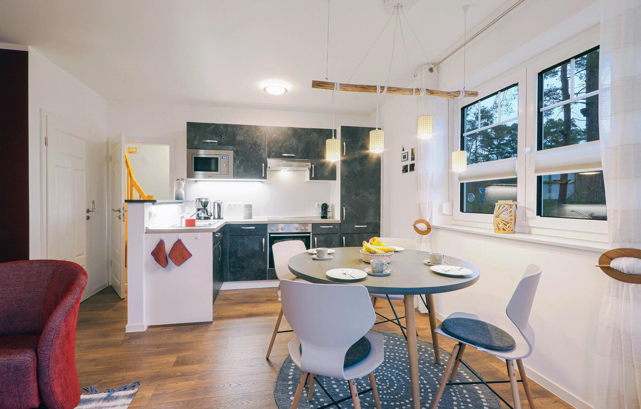A modern kitchen with dark cabinets, a microwave, and a coffee machine. There is a dining area with a round table and two chairs.