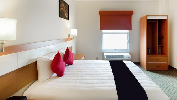 A hotel room with a bed, bedside lamps, a window with a blind, a wardrobe, and a wall-mounted picture.
