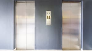A pair of closed elevator doors in a modern building with a control panel above them.