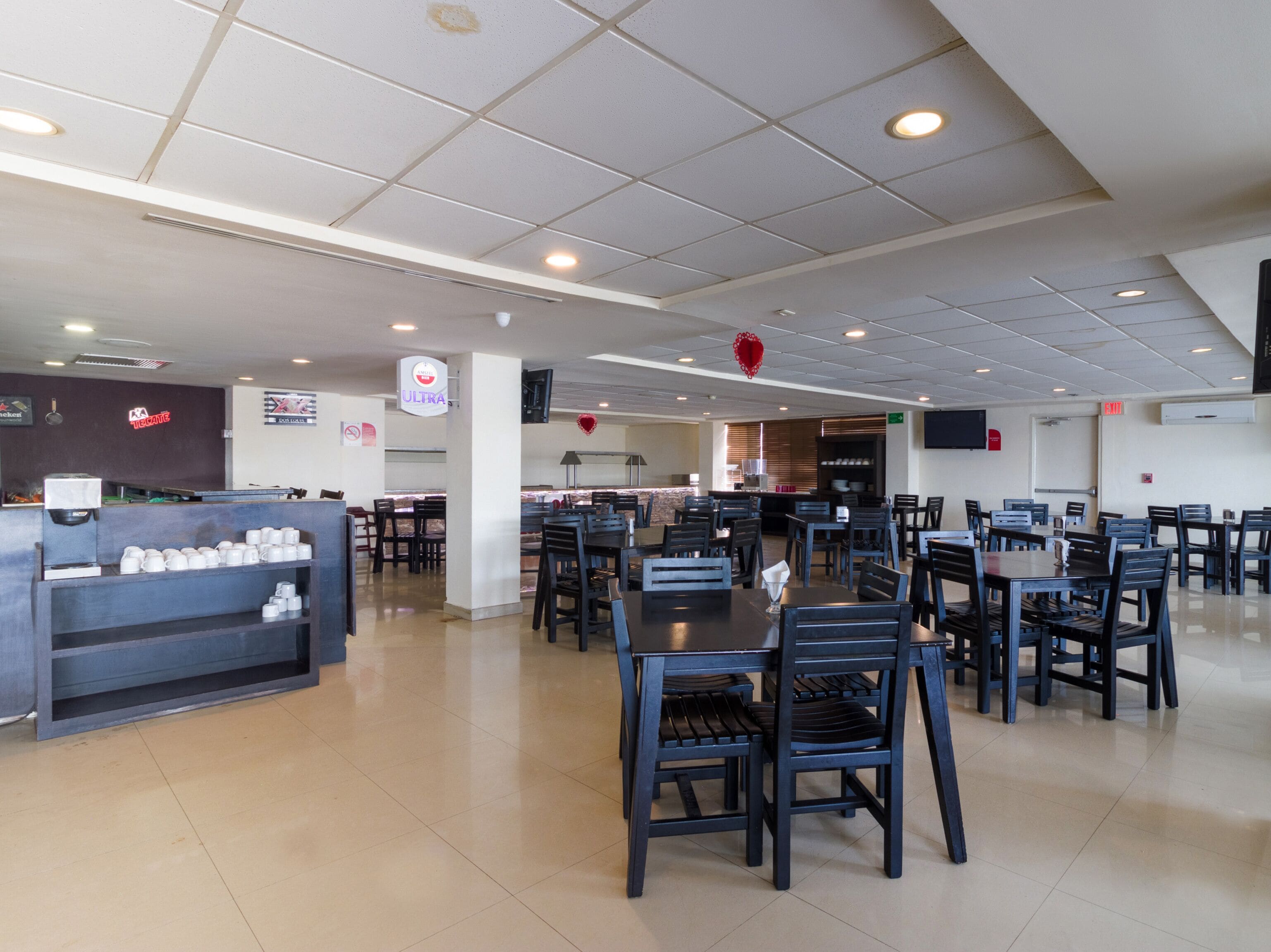 A spacious restaurant with multiple dining tables and chairs, a coffee station, and a kitchen area.